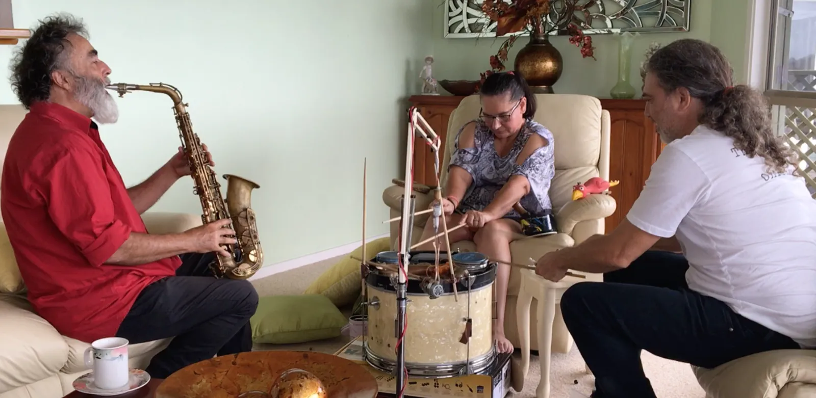 Musicians play saxophone and percussion in a family living room while a woman plays a drum
